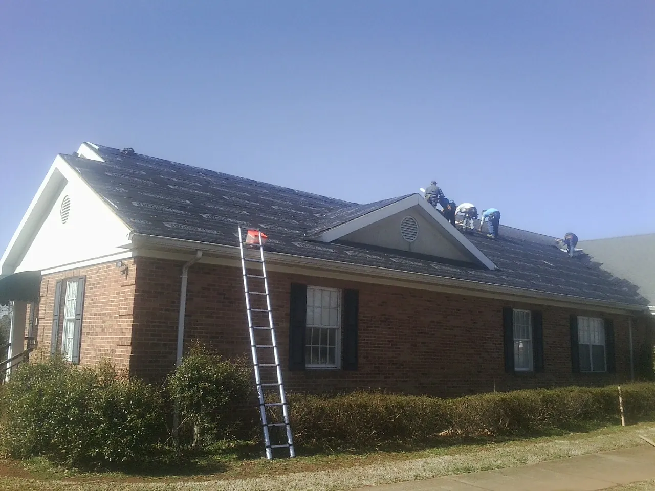 Crew tearing shingles off a brick ranch roof with a ladder set — Metal Roof Repair work by our crew in Brock