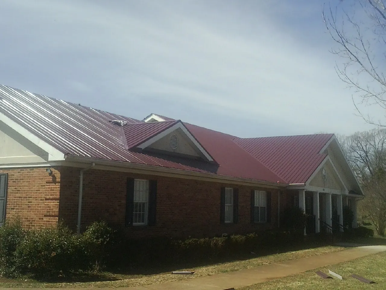 Red metal roof with gabled entries on a long brick building, from a Hail Damage Roof Repair job in Brock
