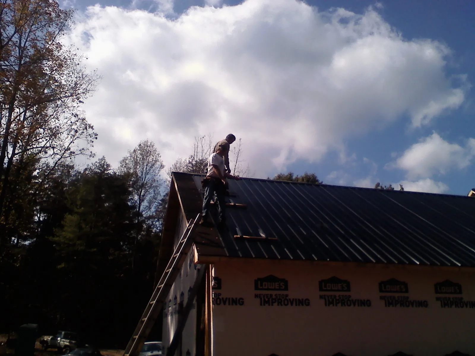 Roofer fastening dark metal panels high against a cloudy sky, from a Roof Inspection job in Brock