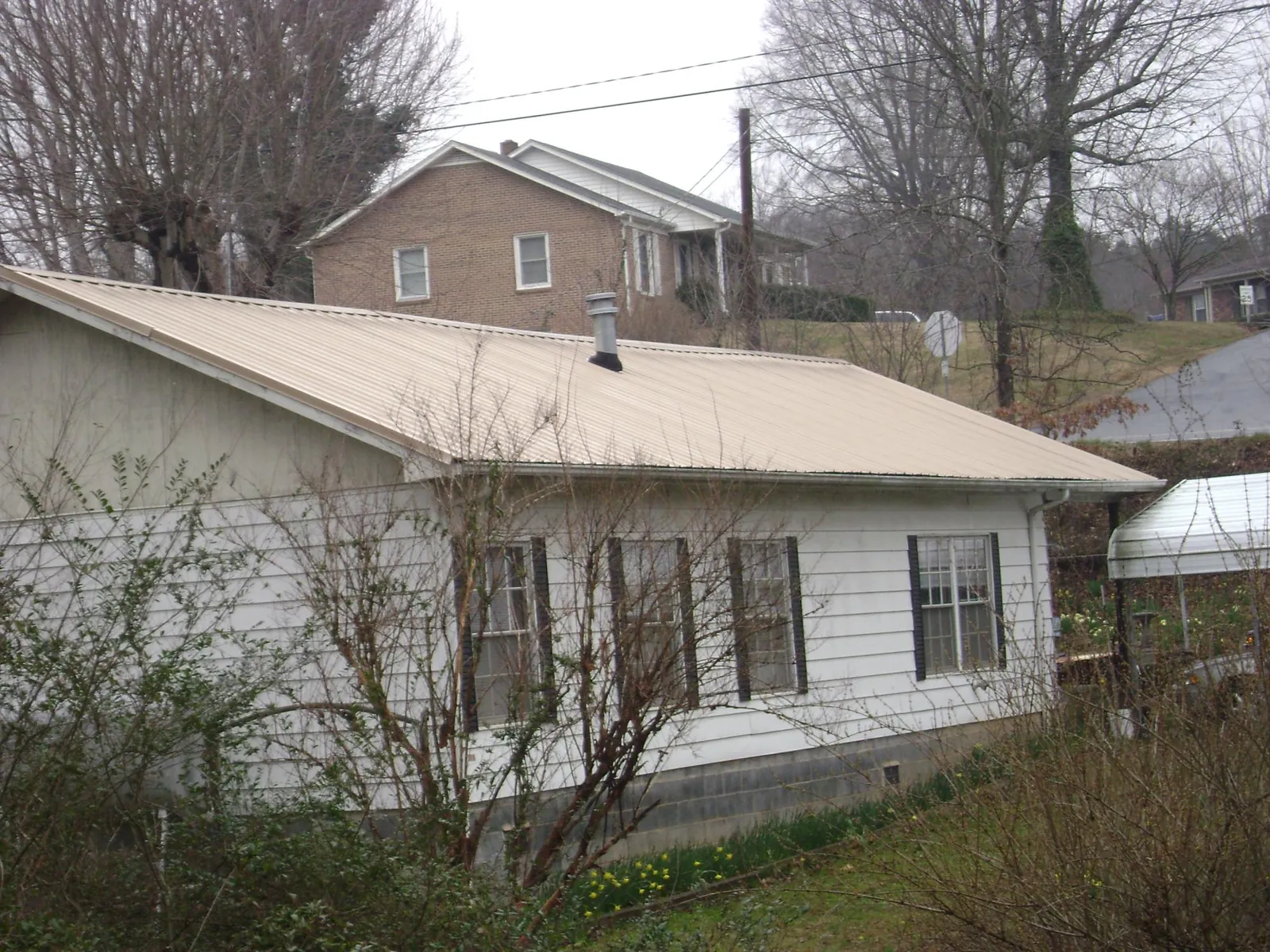 Tan metal roof on a white sided house set into a hillside — Commercial Roofing by Roofing Brothers in Brock