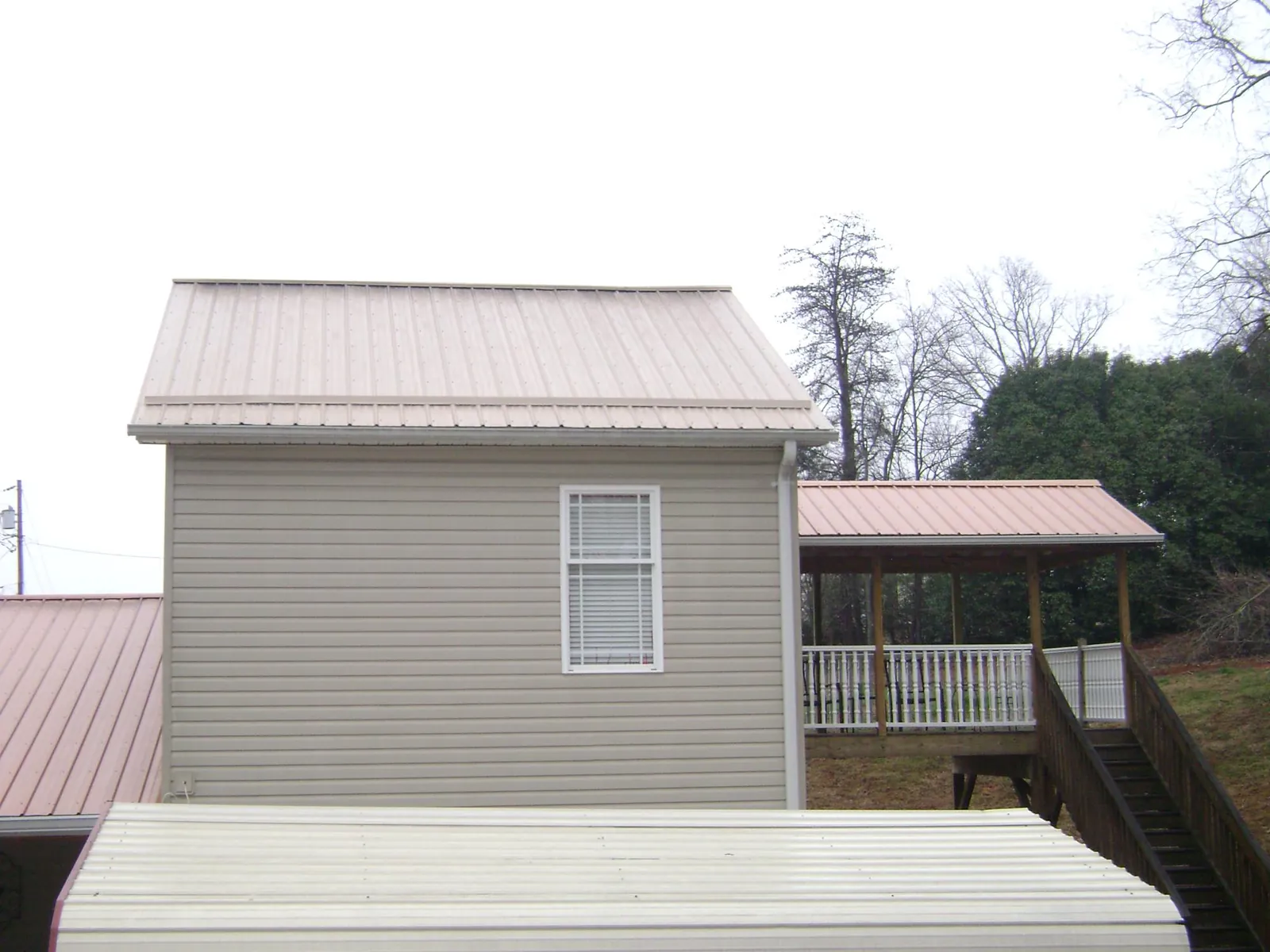 Tan metal roofs on a two story addition and attached porch, from a Roof Replacement job in Brock